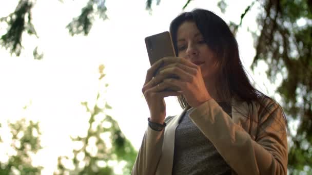 Jonge brunette vrouw typen berichten in openbare chat in sociaal netwerk buiten in het bos — Stockvideo