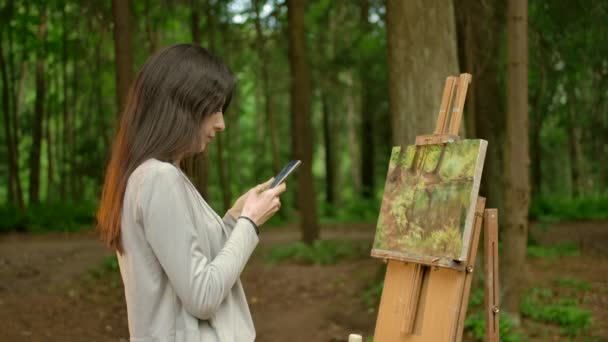 Девушка-художник закончила работу над своей картиной и поболтала в своем смартфоне — стоковое видео