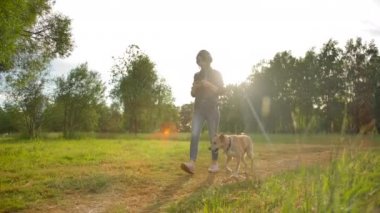 Kulaklıklı bir kız köpeği ile parkta yürür. Ön geniş yavaş çekim görünümü.