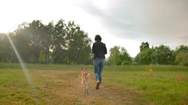 Kulaklıklı çekici bir kadın köpeğiyle parkta yürüyor..