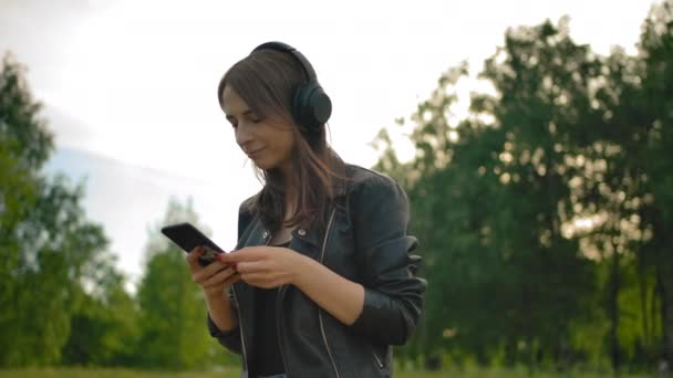 Porträtt av en flicka, lyssnande musik från wi-fi-hörlurar, promenader i parken med sin hund. — Stockvideo