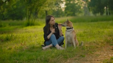 Kotlu ve siyah deri ceketli bir kadın, şehir parkında köpeğini okşuyor..