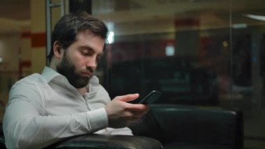Genç erkek, saçını kestirmek için beklerken cep telefonundan sosyal ağları kontrol ediyor..