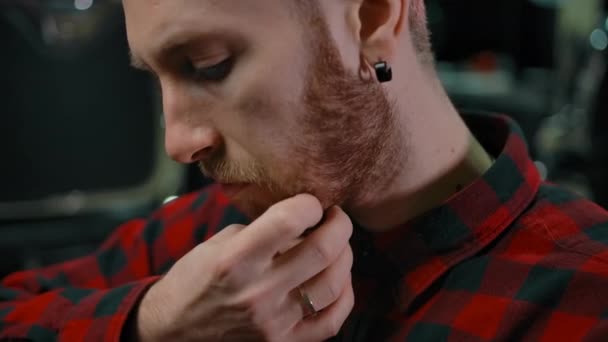 Młody facet dotyka brody przed fryzjerem w salonie fryzjerskim — Wideo stockowe