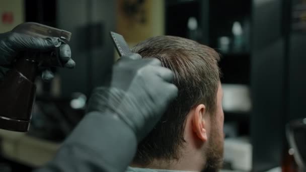 Seorang tukang cukur dalam sarung tangan menyisir rambut dan mengisap keluar dari semprotan — Stok Video