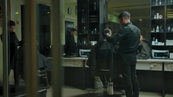 Två klienter och två frisörer frisyr i en mörk frisör rum. — Stockvideo