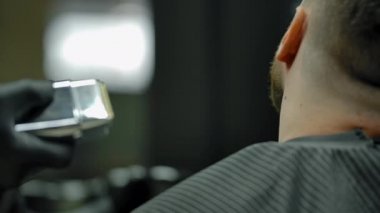 Tanımlanamayan bir adam tıraş makinesiyle müşteri sakalını tıraş ediyor..