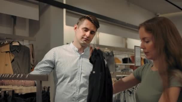Молодая влюбленная пара выбирает одежду в магазине — стоковое видео