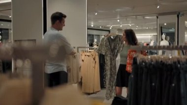 Mağazadaki beyaz kadın, erkeklerin iki elbise arasından seçim yapmalarını istiyor.