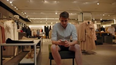 Bir giyim mağazasında sosyal ağları karıştıran beyaz bir adam.