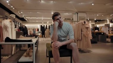 Sıkılmış bir adam giyim mağazasında bir bankta oturuyor.