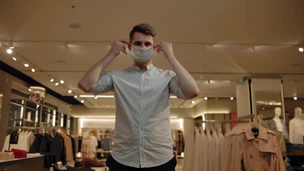 Een jongeman zet een masker op zijn gezicht in een kledingwinkel. — Stockvideo