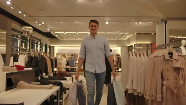 Alışveriş paketleriyle bir adam kameraya gülümseyerek yaklaşıyor.. — Stok video