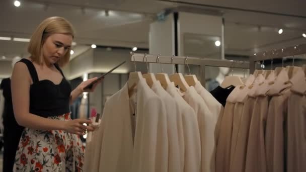 Wanita pirang kaukasia memeriksa pakaian di toko — Stok Video