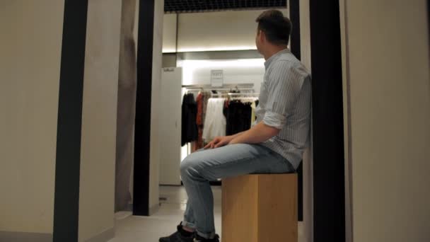 Joven chico esperando su novia atando nuevo vestido en probador — Vídeos de Stock