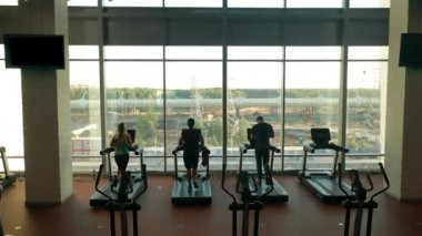 Üç sporcu, iki erkek ve bir kadın spor salonunda koşu bandında koşuyor.