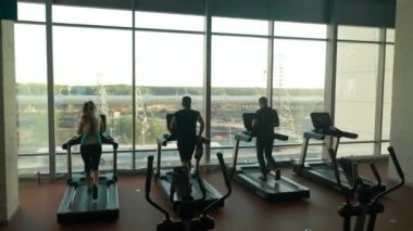 Spor salonunda koşu bandında koşan üç sporcunun arka plan görüntüsü.