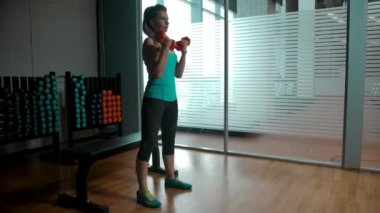 Kafkasyalı sarışın kadın spor salonunda iki dambılı olan pazılar için egzersiz yapıyor.