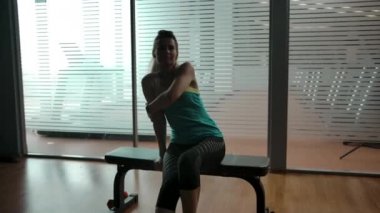 Kız spor salonundaki bir bankta dinleniyor ve antrenmandan sonra omzunu ısıtıyor.