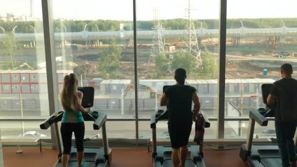 Drie sporters, twee mannen en een vrouw rennend op loopbanden in een sportschool — Stockvideo