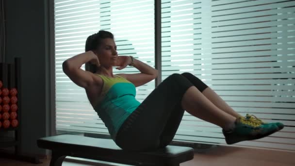 A menina faz exercícios abdominais em um banco no ginásio ao lado de uma grande janela — Vídeo de Stock