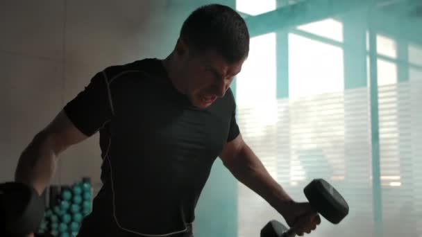 Caucásico macho apenas haciendo ejercicio con pesadas mancuernas en ahumado gimnasio — Vídeos de Stock