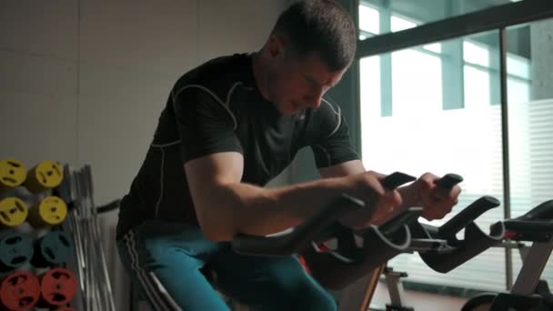 An active male athlete pedals on a stationary bike in a sports hall — Stock Video
