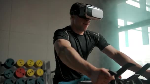 Επαγγελματίας αθλητής εκτελεί αθλητική άσκηση σε προσομοιωτή ποδηλάτων σε κράνος VR — Αρχείο Βίντεο