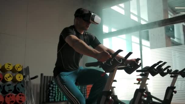 Sportig hane som tränar tungt på cykelsimulator i VR-hjälm — Stockvideo