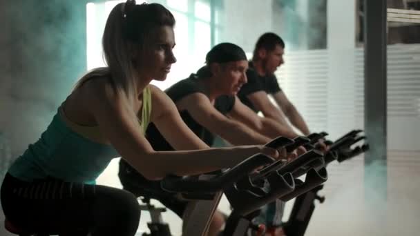 Sportowcy trenują mięśnie nóg na rowerze treningowym w siłowni z rzędu — Wideo stockowe