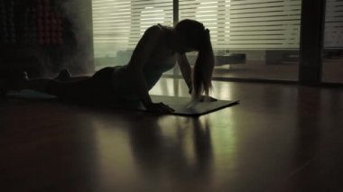Spor salonunda yoga yapan seksi bir kadının silüeti spor halısı üzerinde.
