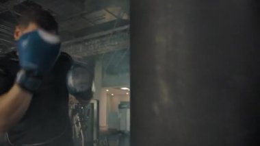 Modern spor salonunda yumruk torbası takan beyaz bir sporcunun yan görünüşü.