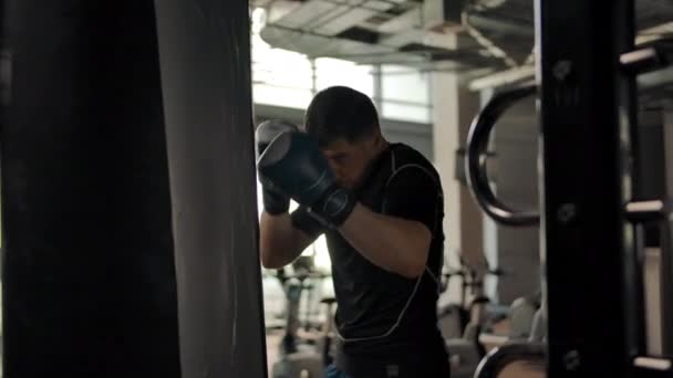 Primer plano de un agresivo hombre caucásico golpeando un saco de boxeo en un gimnasio — Vídeos de Stock