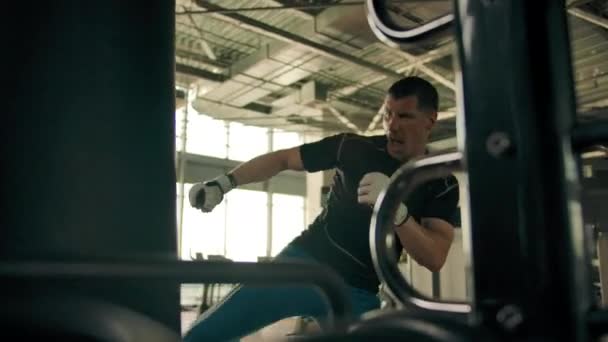 Hombre en ropa deportiva golpeando duro en el saco de boxeo en el gimnasio — Vídeo de stock