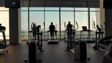 Boş bir spor salonunda koşu bandında koşan tanınmayan üç kişinin siluetleri.