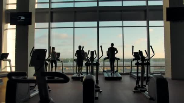 Tres personas irreconocibles corriendo en cintas de correr en un gimnasio vacío — Vídeos de Stock