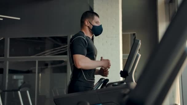 Un atlet profesionist într-o mască de protecție rulează pe o bandă de alergat în sala de sport — Videoclip de stoc