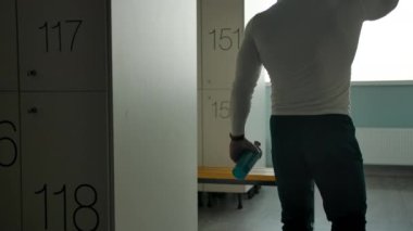 Bir erkek soyunma odasına girer ve dinlenmek ve su içmek için bankta oturur.