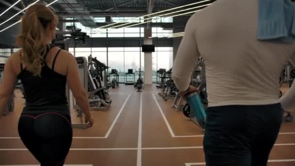 Un par de atletas van a través del gimnasio a las máquinas de ejercicio — Vídeos de Stock