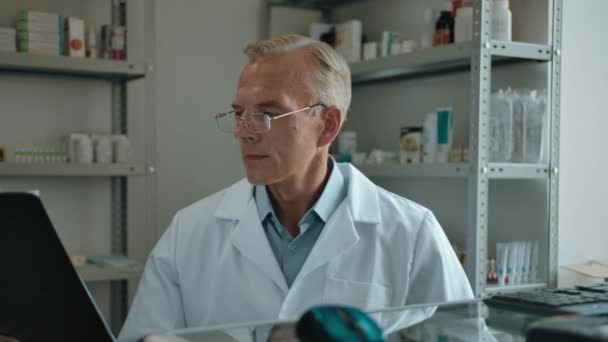Gammal läkare apotekare i vit rock mantel och glasögon tittar på en text tablett — Stockvideo