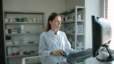 Kafkasyalı kadın bilgisayardan siparişleri kontrol ediyor ve ilaçlarla rafa kaldırıyor.