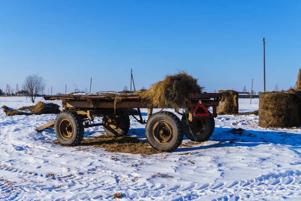 Un carro viejo y los restos de los rollos de heno en un campo en invierno . — Foto de Stock