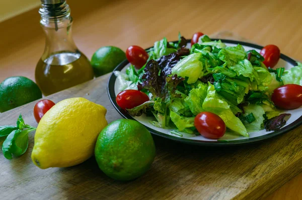 Fresh salad from different types of greens and cherry tomatoes, seasoned with olive oil and lime juice with lemon.