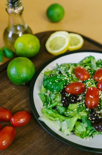 Färsk sallad från olika typer av greener och en körsbärs tomat, klädd med olivolja och bevattnas med sesamfrön. — Stockfoto