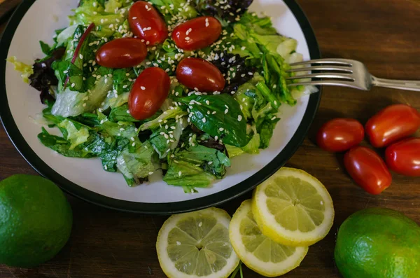 Świeża sałatka z różnych rodzajów zieleni i pomidorem wiśniowym, ubrana w oliwę z oliwek i posypana sezamem. — Zdjęcie stockowe