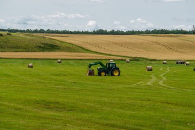 Bir traktör başka bir traktör bir römork üzerine saman balya yükler.