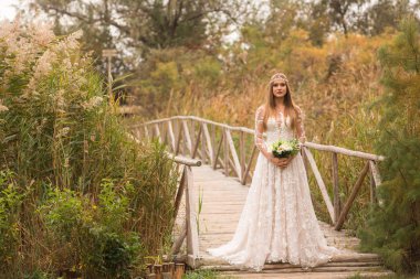 Buket çiçek ahşap köprü ve uzun otların önünde poz ile sarı gelin