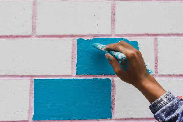 Painter\'s hand holding a brush while painting on a wall with blue color.