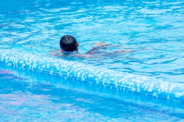 Parlak mavi bir havuzda yüzen bilinmeyen kişi.