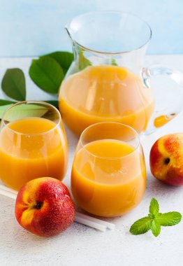 Şeftali suyu gözlük ve bir sürahi ve yaprakları bir tablo ile taze şeftali. mavi arka plan. kopya alanı